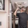 RVTechnician Replacing Air Condition Filter Inside Travel Trailer. Recreational Vehicles and Travel Industry.