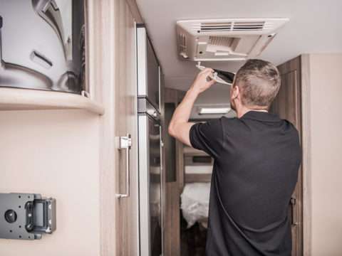 RVTechnician Replacing Air Condition Filter Inside Travel Trailer. Recreational Vehicles and Travel Industry.